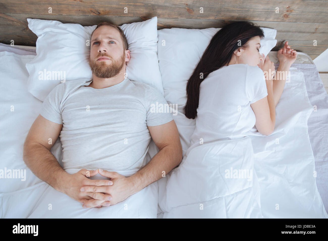 Young man looking at ceiling while his wife sleeping Stock Photo