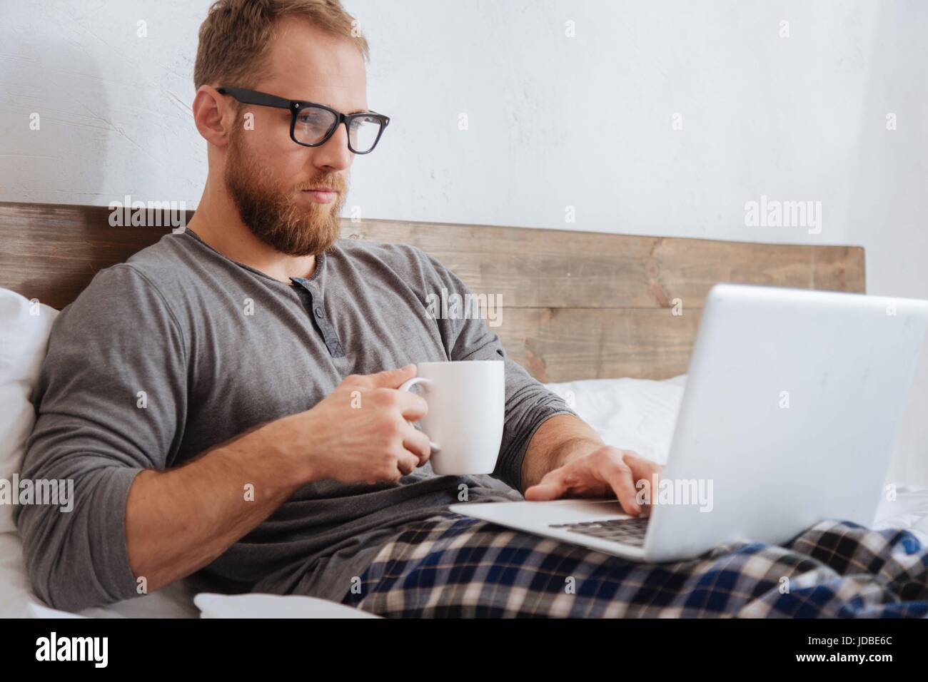 Handsome bearded man working with laptop in bed Stock Photo