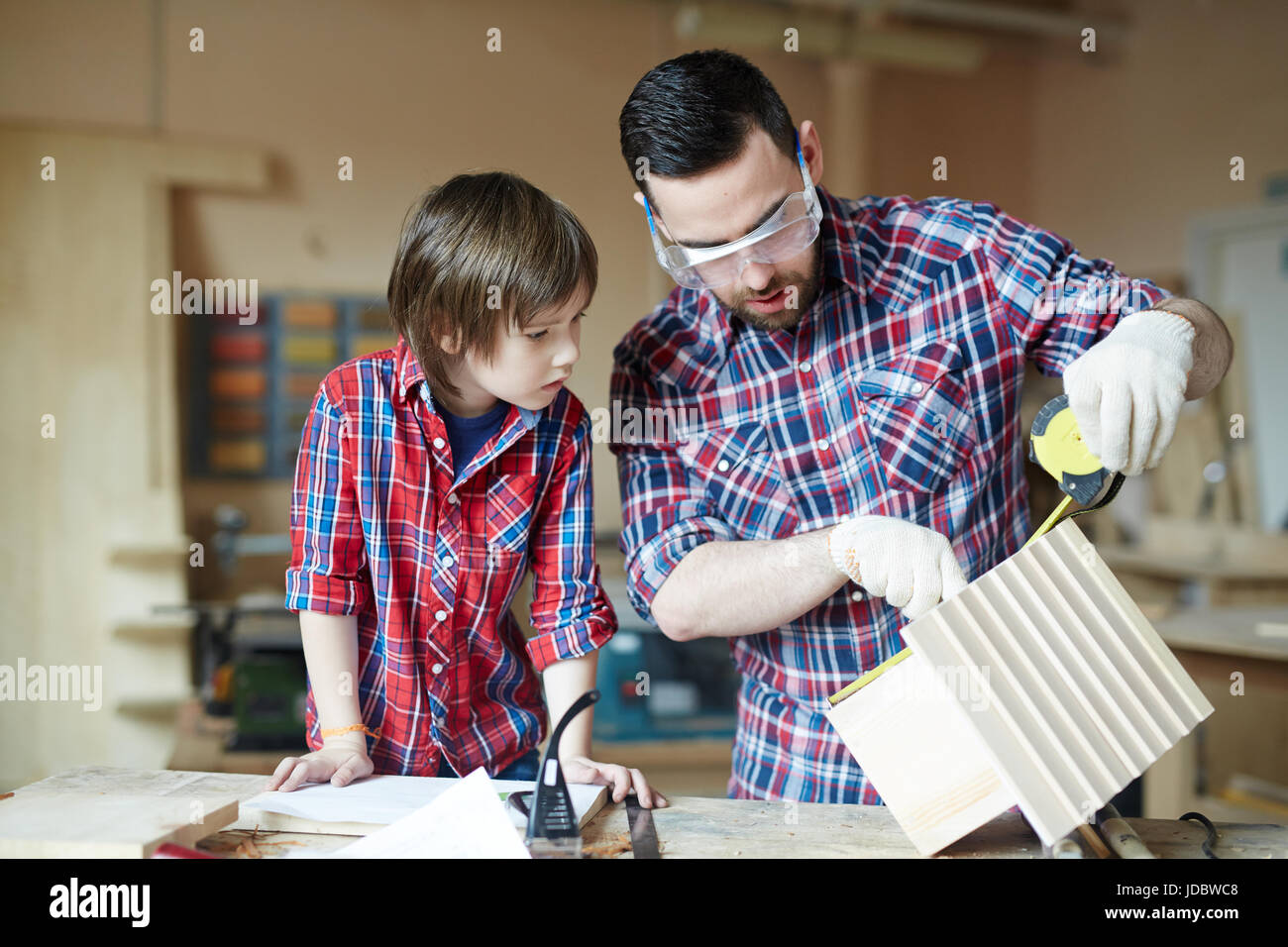Little boy and his father measuring height of starling-house in workshop Stock Photo