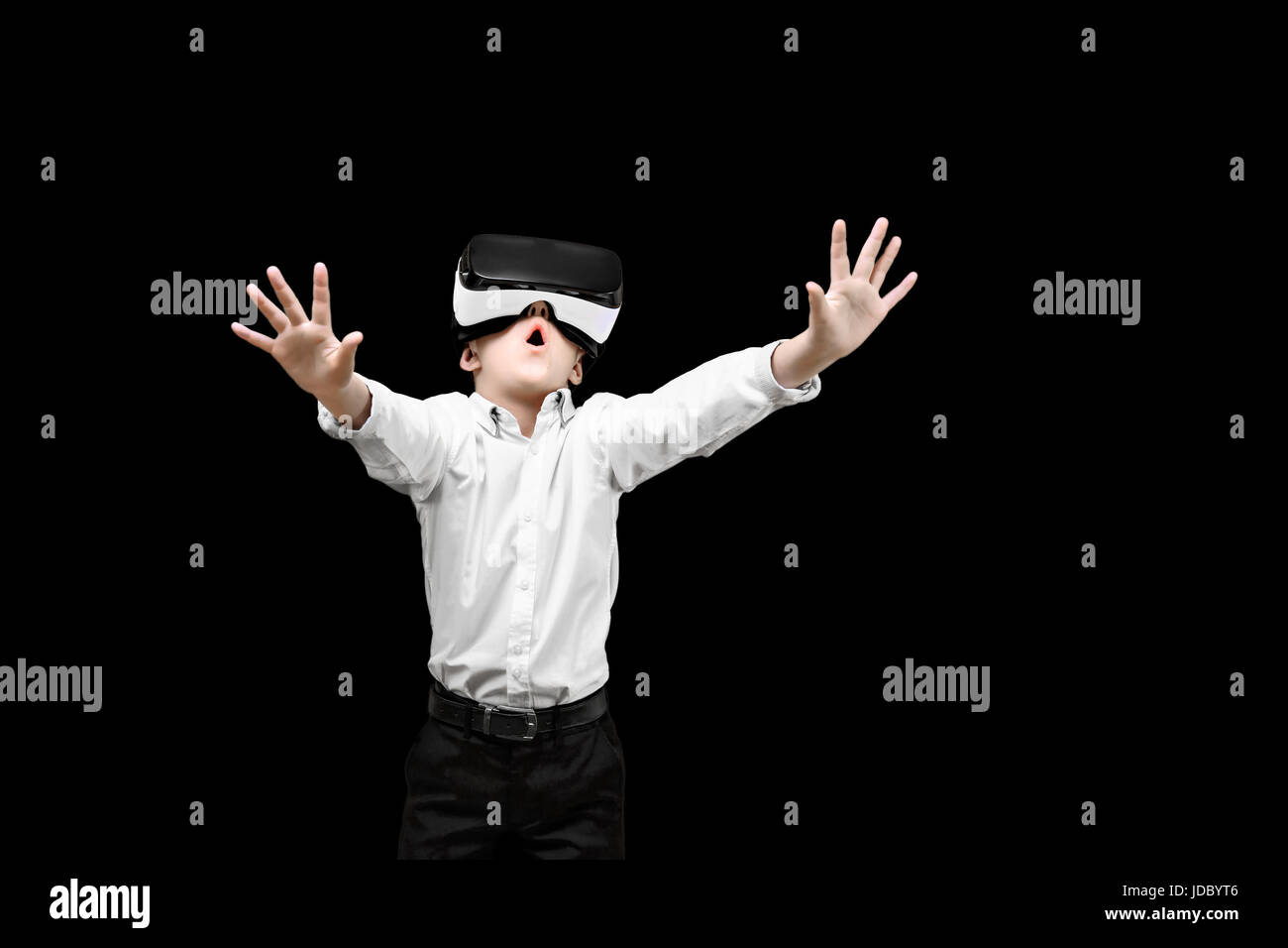 Kid in formal outfit wearing VR glasses putting hands out in excitement isolated on black background. Stock Photo