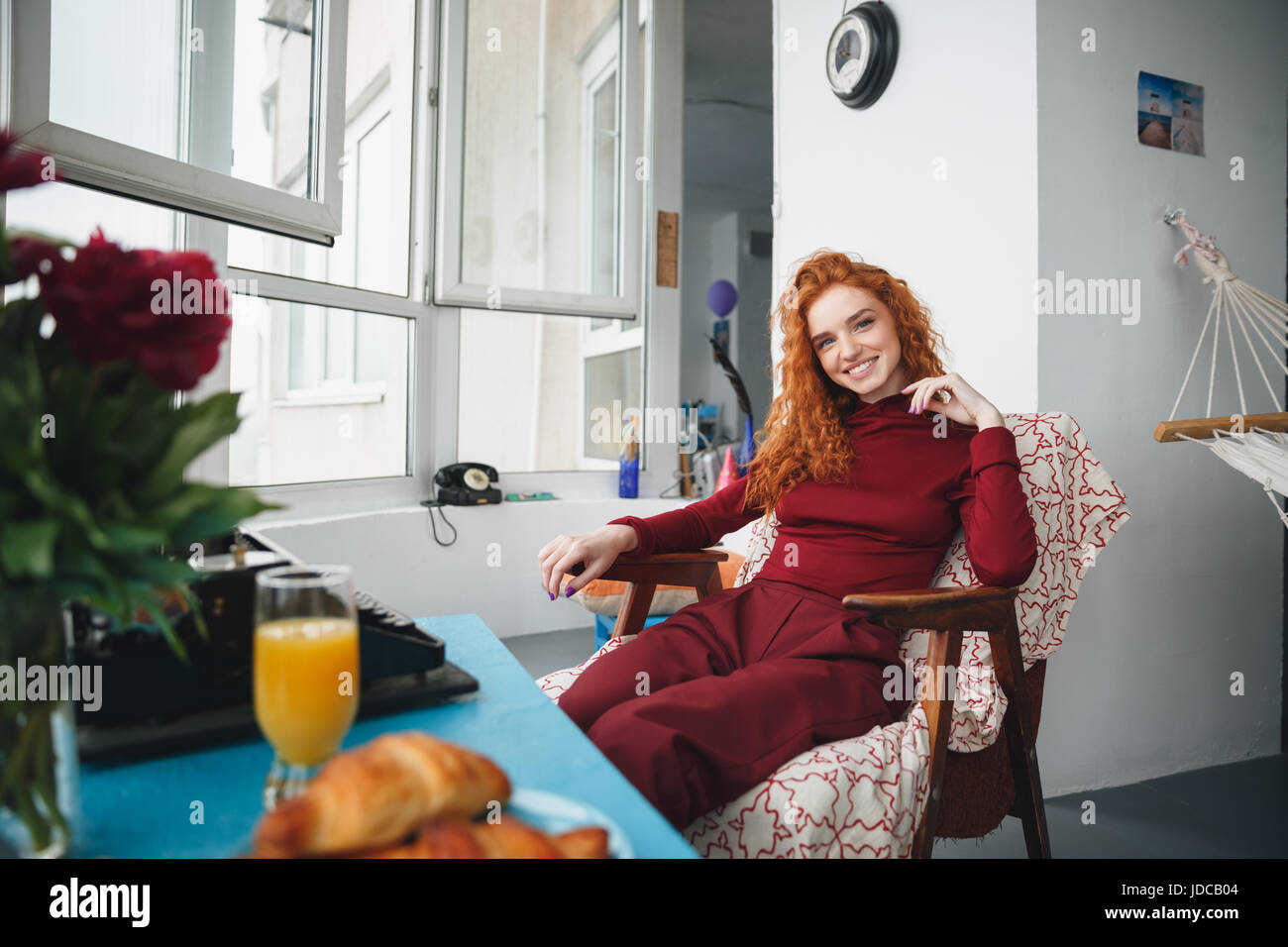 Portrait of a smiling pretty girl sitting on a chair at home and ...