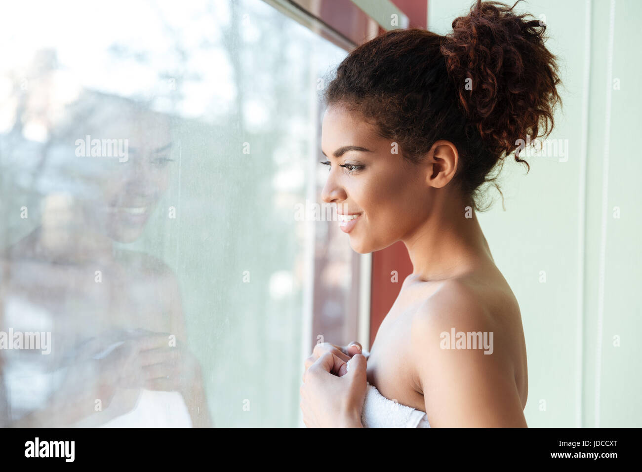 Image of smiling young african woman dressed in towel standing at home ...