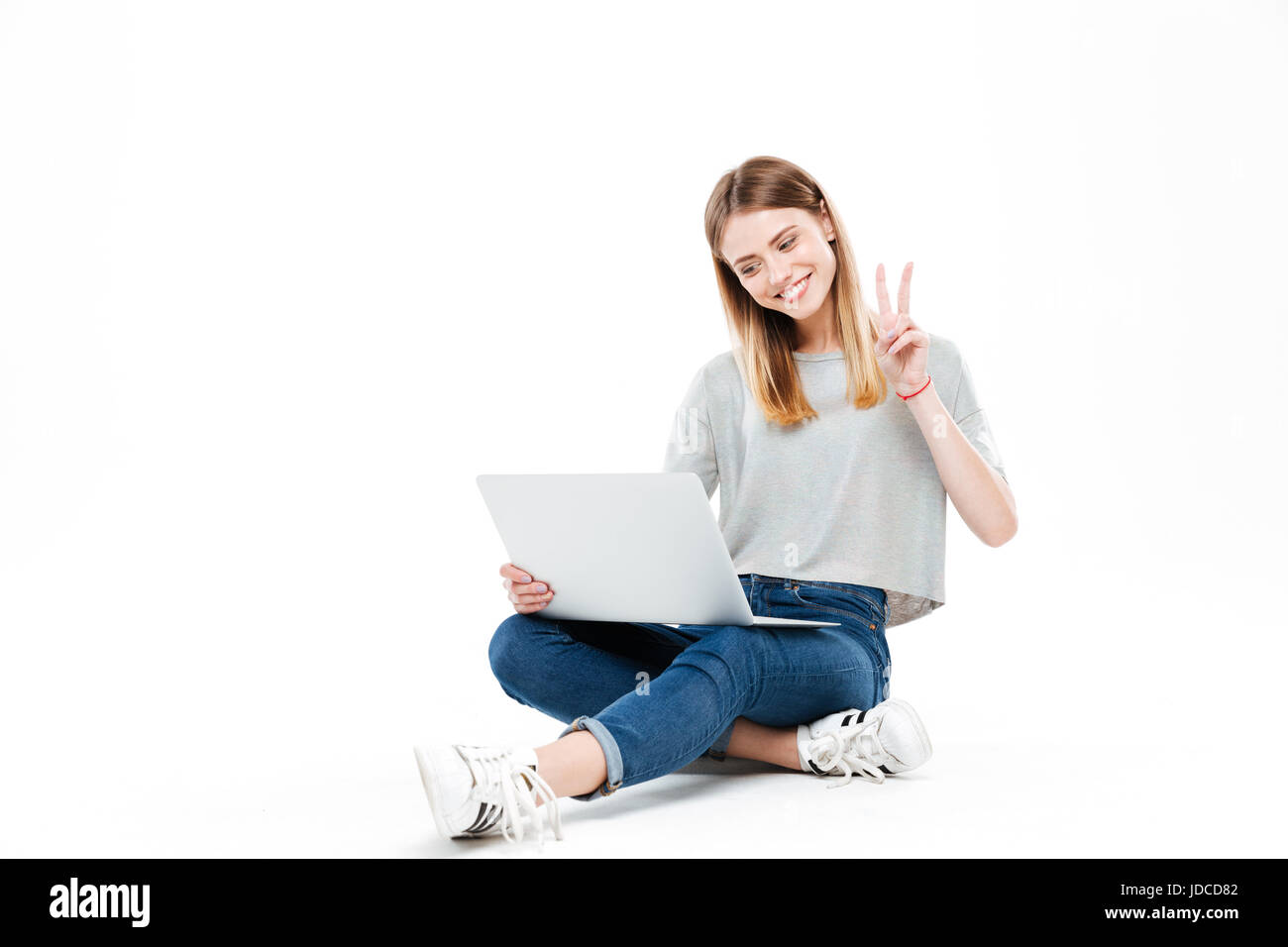 Young smiling woman using laptop computer and shoing peace gesture isolated over white Stock Photo
