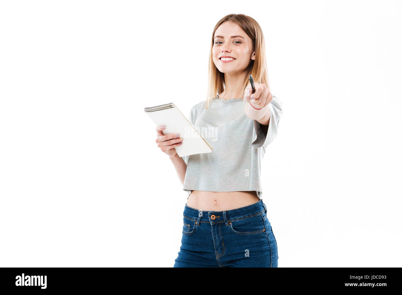 Portrait of a cheerful young girl holding notepad and pointing pen at ...