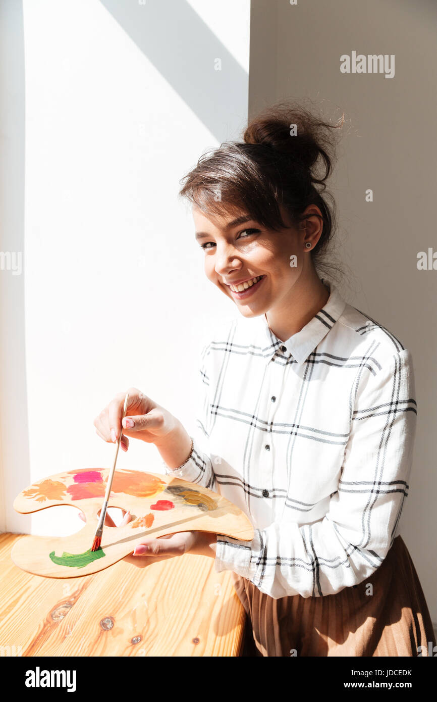 Smiling pretty woman artist holding palette and looking at camera in ...