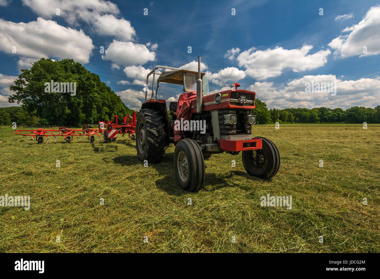A tractor with a hay tedder standing on a field after tedding the grass for the preparation of hay on a hot summer day in the Netherlands Stock Photo