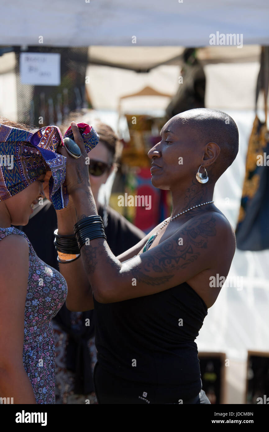 Young black woman with cropped hair fixing an African head scarf/wrap to a young girl at the Africa Oye music festival in Liverpool Stock Photo