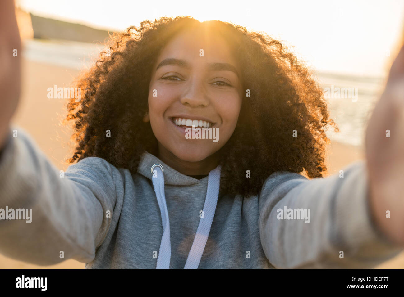 Outdoor portrait of beautiful happy mixed race African American girl teenager female young woman on a beach taking a selfie photograph smiling laughin Stock Photo