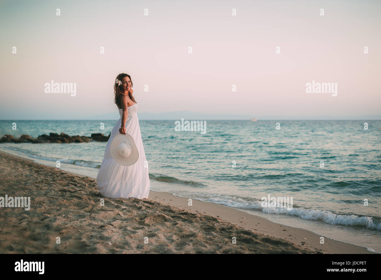 Beautiful young smiling woman in white dress walking on the beach and ...