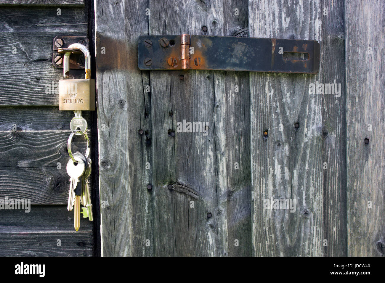 Black hasp and staple or clasp, with padlock and keys. The garden shed door is unlocked and the keys are still in the lock. The staple, clasp is open Stock Photo