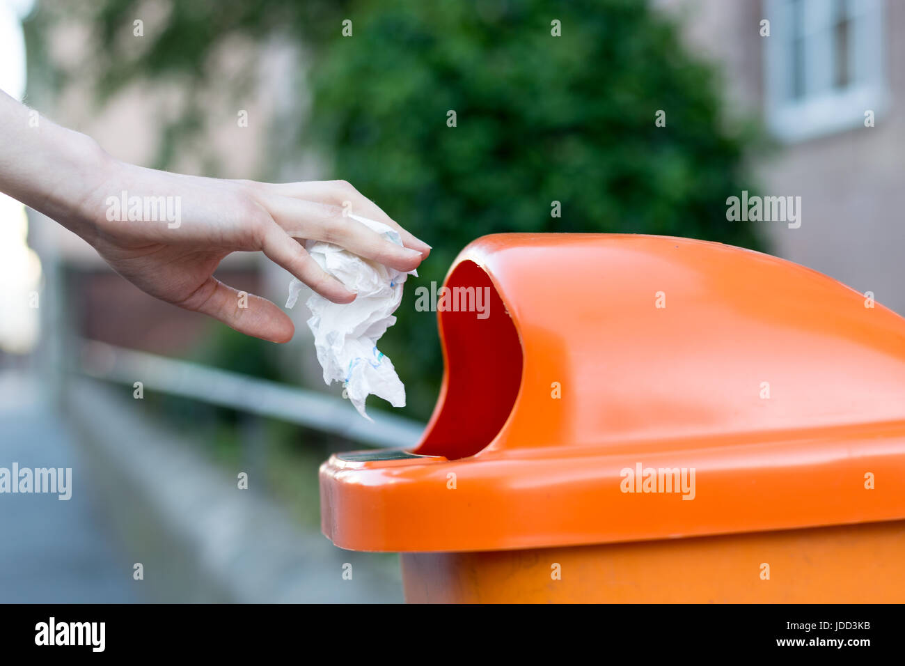 Throwing waste into a an orange trash can in the street from the side