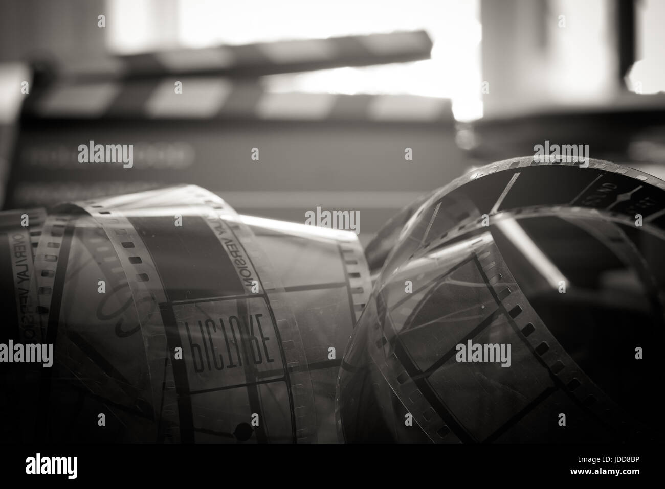 Aged vintage 35 mm film reel, old movie symbol, header filmstrip unrolled close up black and white, defocused clapper board in background Stock Photo
