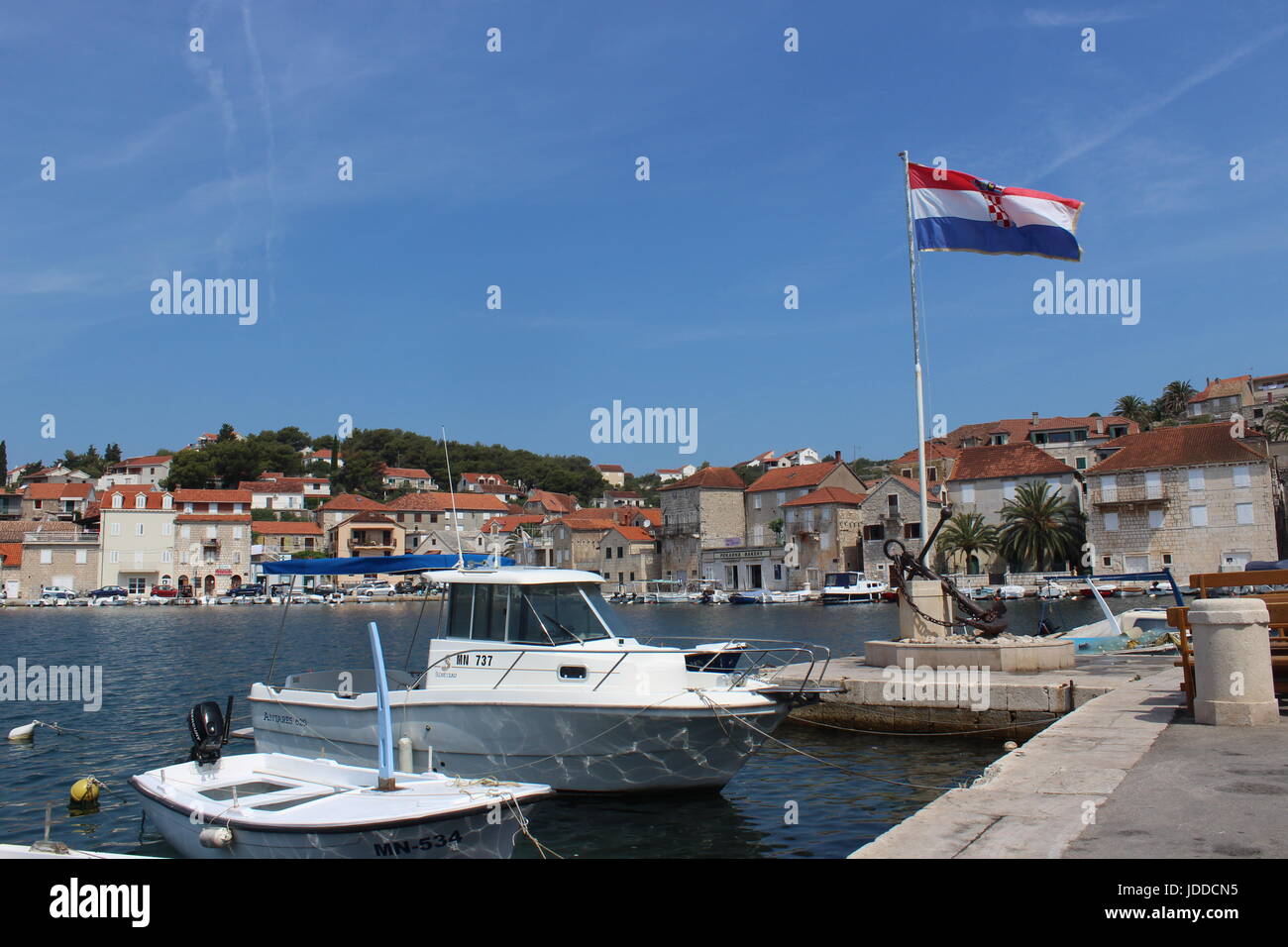 Croatian flag flying at harbourside in bright sunshine with clear blue skies and boats and houses in background Stock Photo