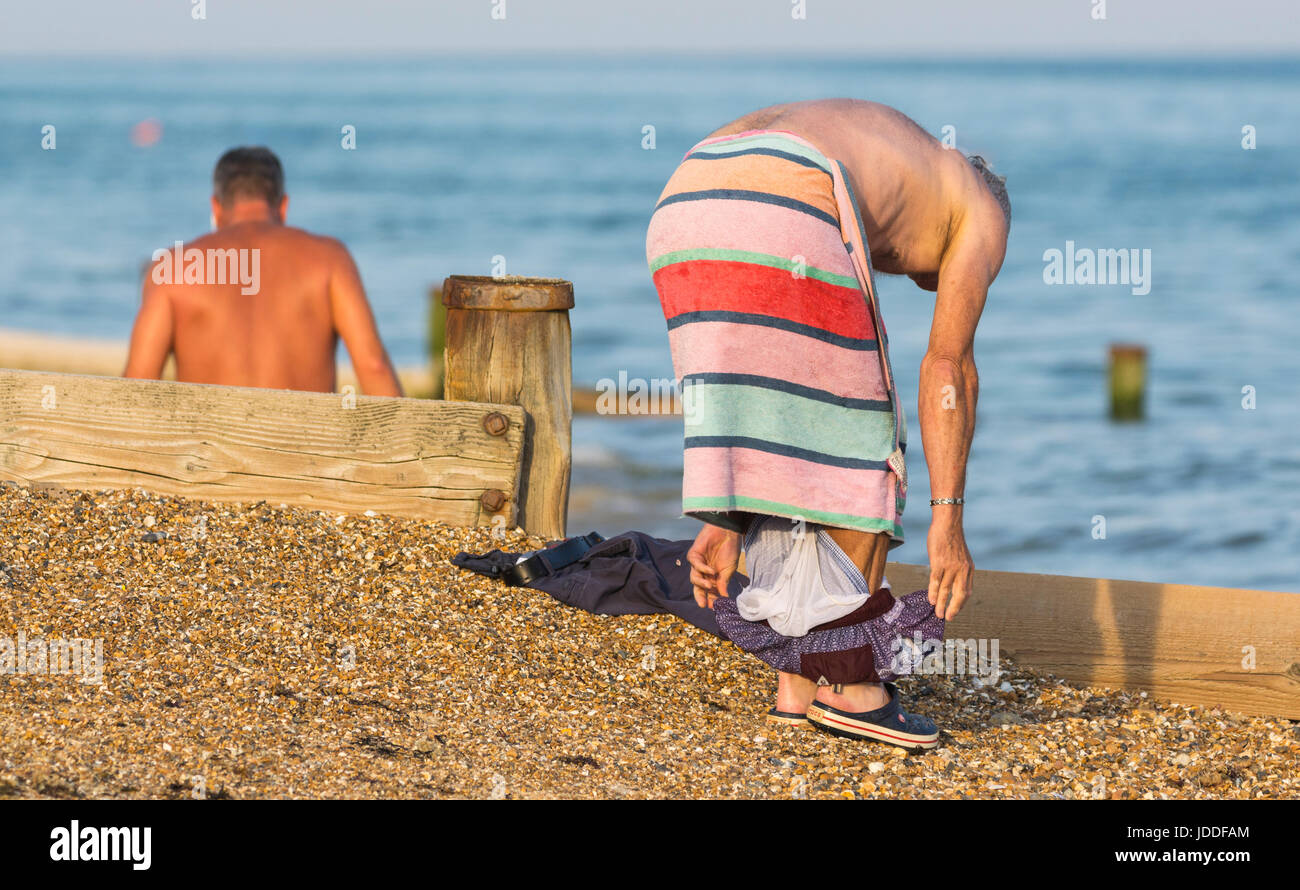 Man on the beach with a towel as he changes out of his swimming trunks. Stock Photo