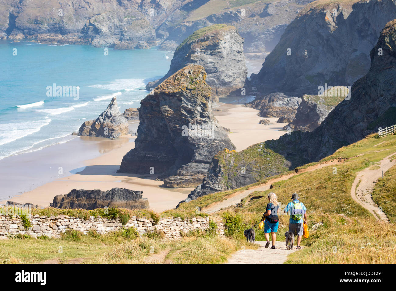 A man and woman couple walking down the path towards the beach at the popular attraction of Bedruthan Steps in Cornwall on a hot summers day part of the National Trust Stock Photo