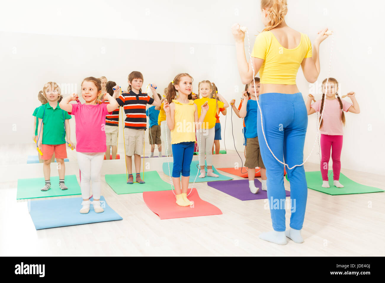 Group of happy kids jumping ropes with sports teacher at gym lesson Stock Photo
