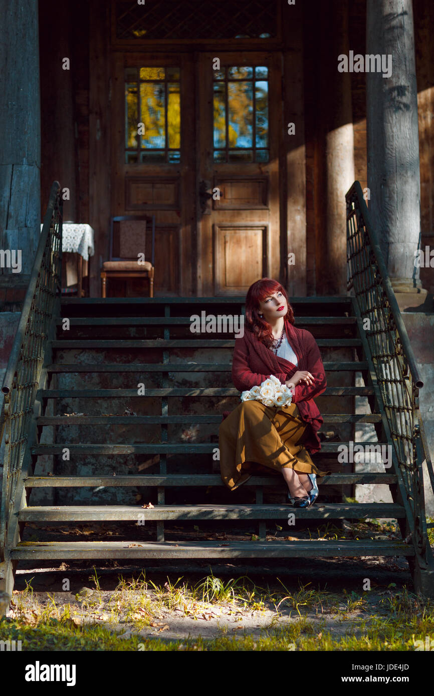 Beautiful young woman in long skirt and wool red scarf sitting on old ...