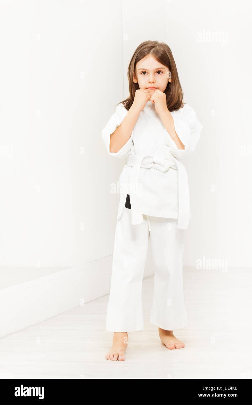 Portrait of six years old girl wearing white kimono standing in karate position in gym Stock Photo