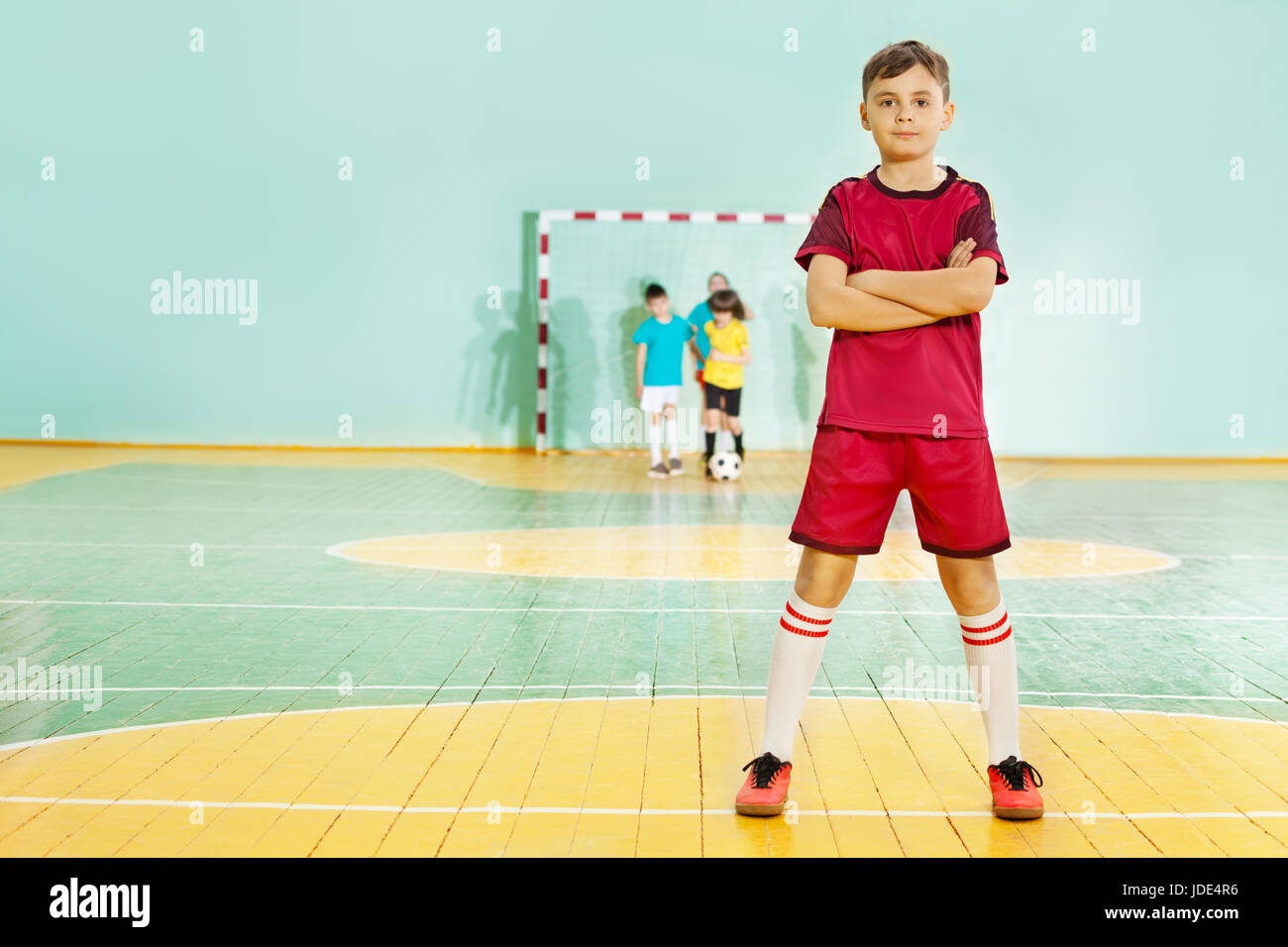 Portrait of 12 years old boy, football player in uniform, standing in sports hall with his arms folded Stock Photo