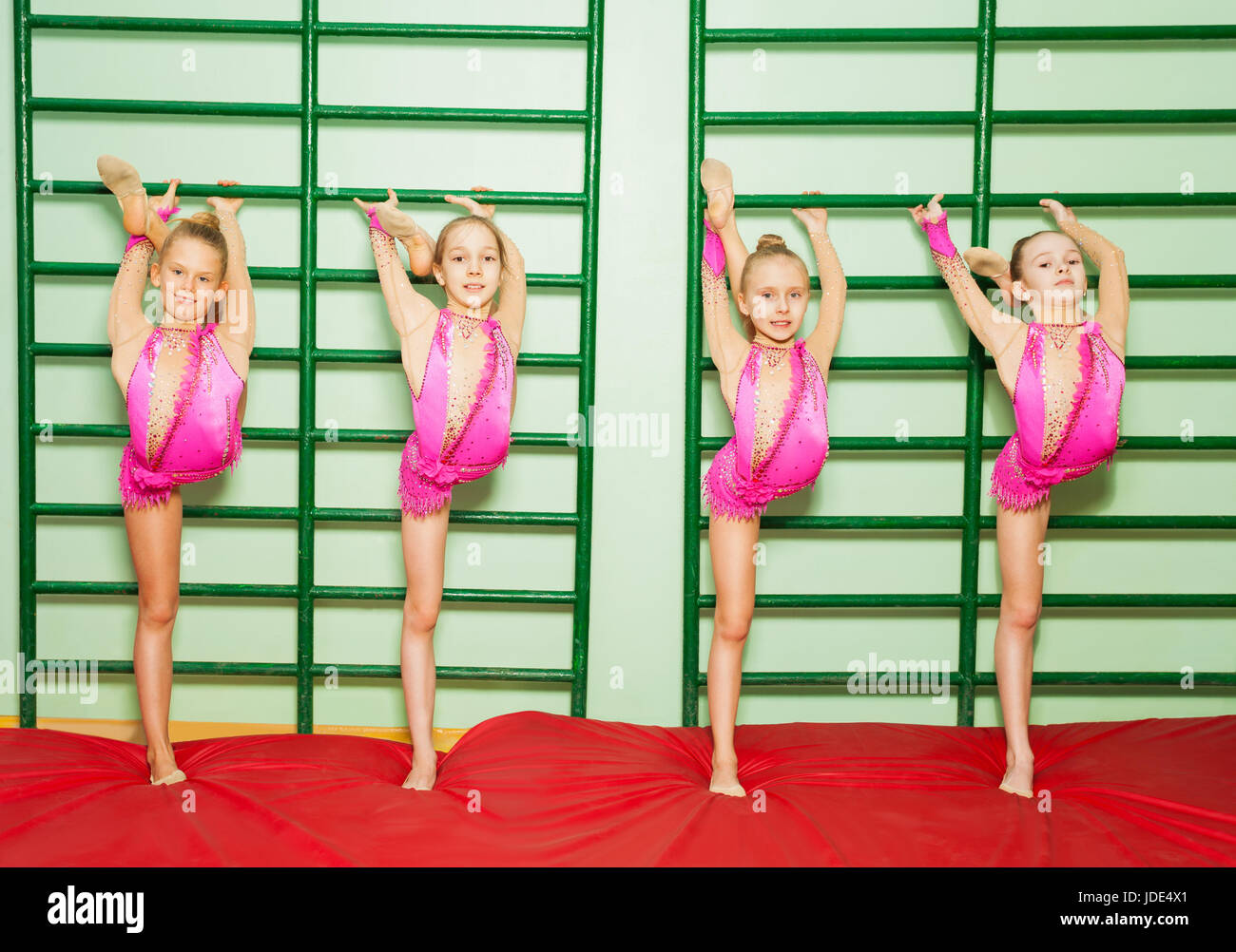 Group of four preteen girls stretching near wall mounted gym ladder during gymnastic class Stock Photo