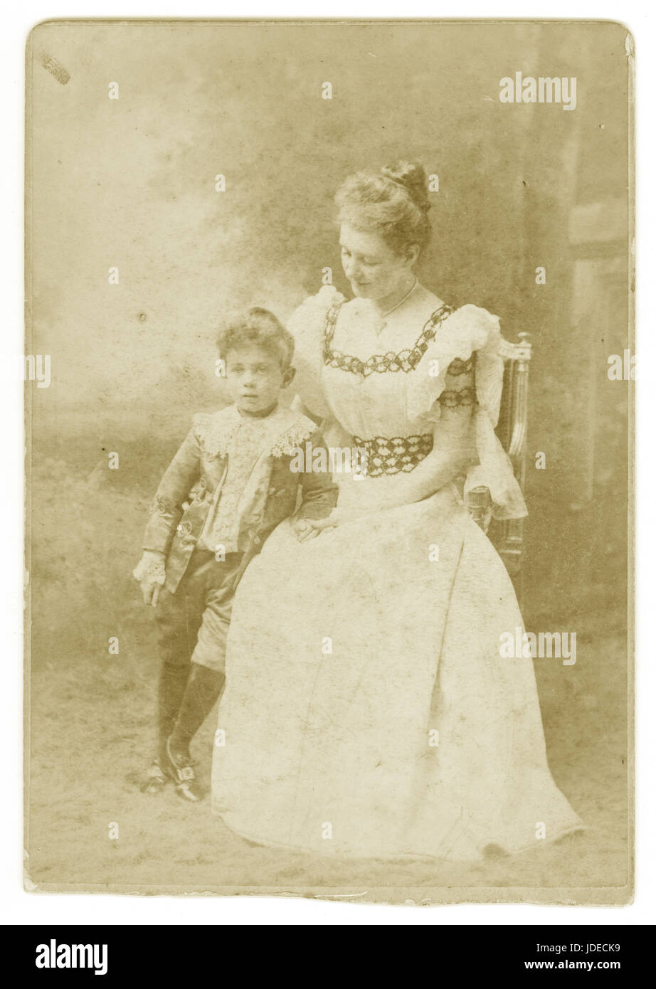Victorian Cabinet card photograph (cropping at base) of an attractive  lady wearing a beautiful summer dress with lace sleeves, proudly holding her son who is dressed in breeches and frilly shirt collar and velvet jacket - a fashion inspired by the Little Lord Fauntleroy novel by Frances Hodgson Burnett.published in 1885–1886. Circa 1890's Stock Photo