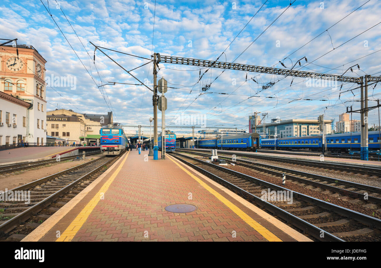 Railway station with blue trains at sunset in summer in Europe. Industrial landscape with railroad, passenger trains, blue sky with clouds in the even Stock Photo