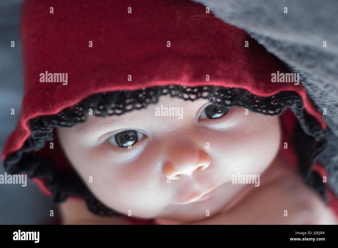 Baby face close up, with big beautiful eyes. Newborn in a red cap. Toddler looking through lace, directly into the lens. Stock Photo