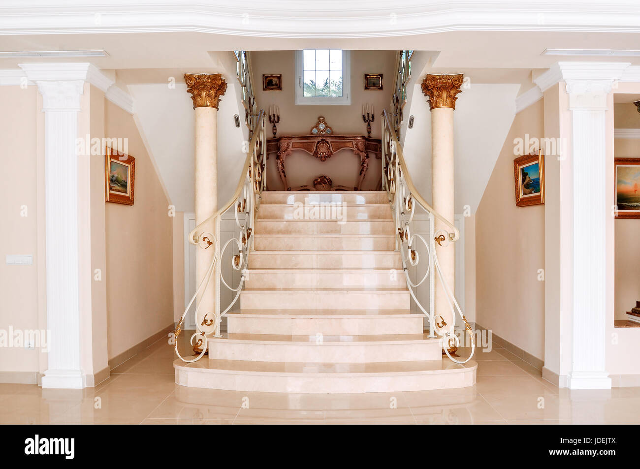 Luxurious staircase with marble steps and decorative and  ornamental iron railings. On the top are decorating furniture in neoclassical style, a table Stock Photo