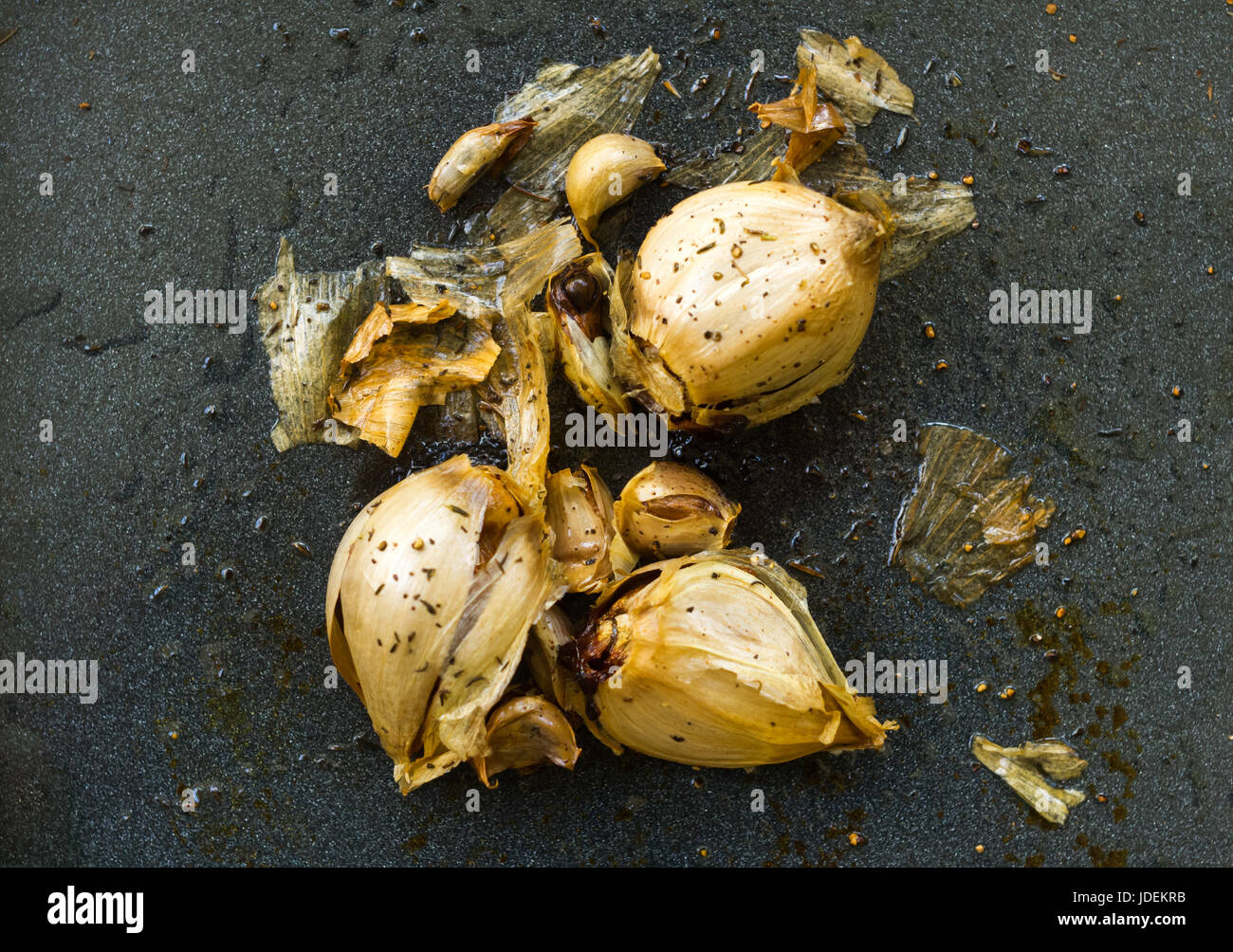 Caramelised roasted garlic fresh out of the oven on a steel blue tray sprinkled with dried rosemary and thyme Stock Photo