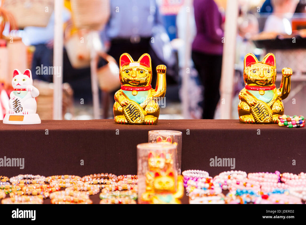 Japanese lucky cat, Maneki-neko, figures on stall. Traditional kneeling cat figure with one arm raised in greeting to welcome customers. Stock Photo