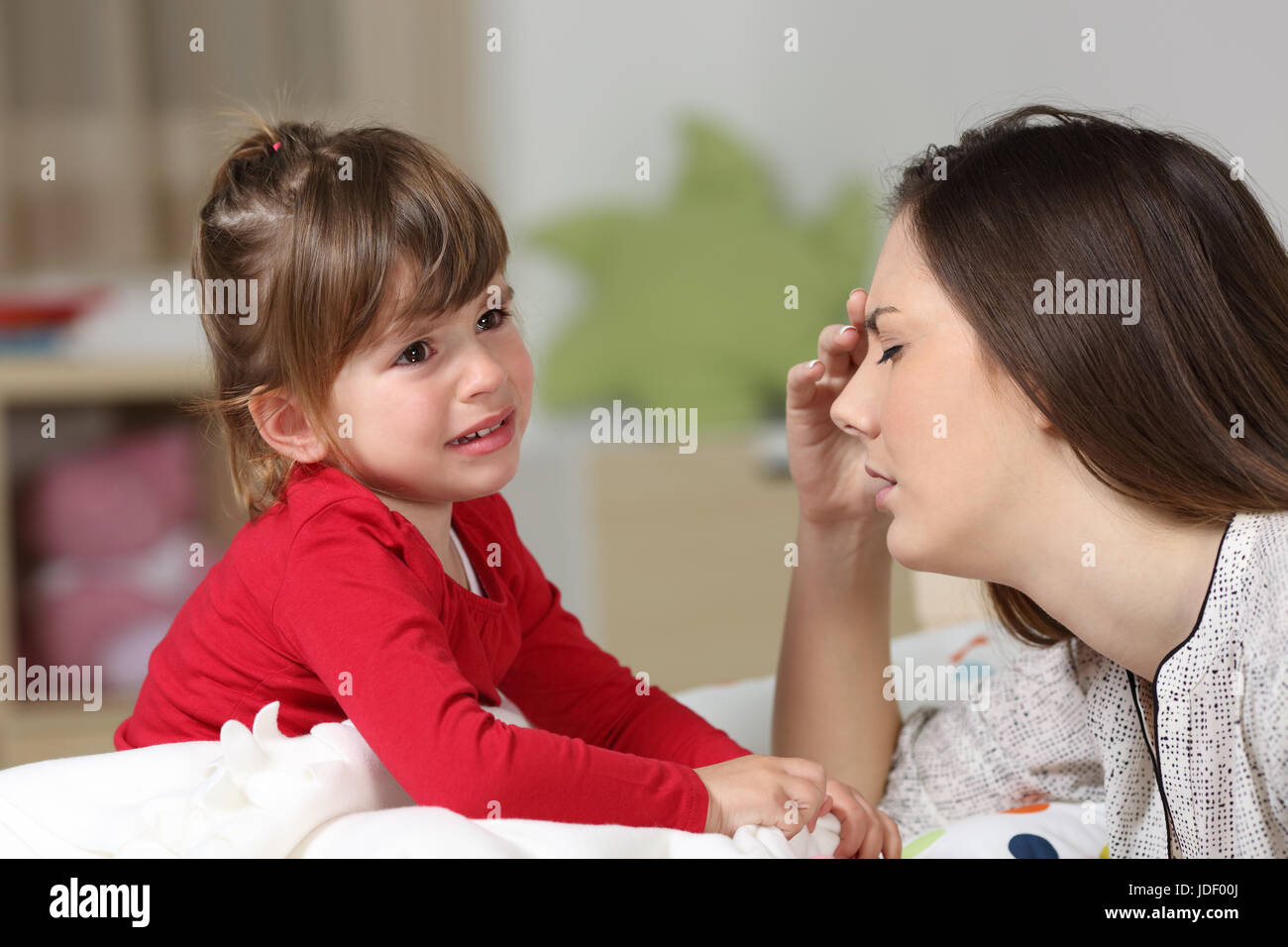 Fed up woman listening to her two years old daughter crying sitting on the bed in a house interior Stock Photo