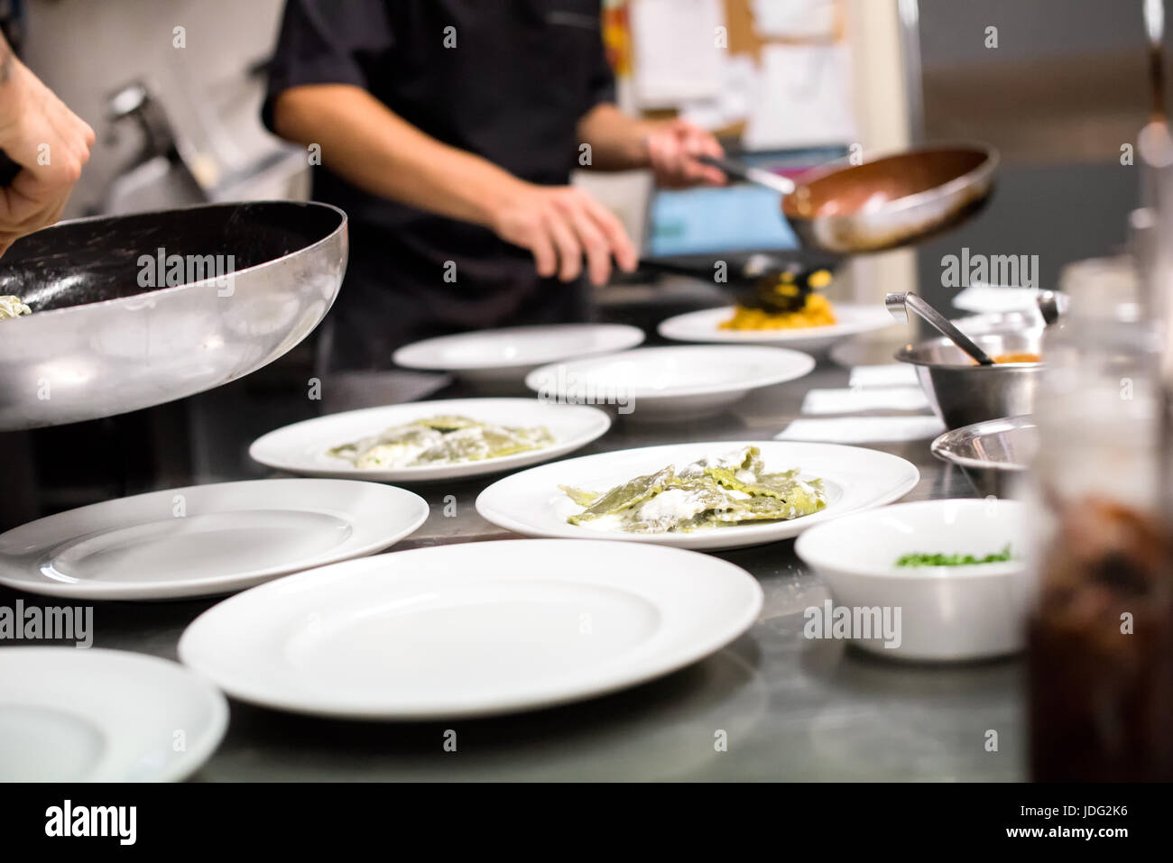 Restaurant kitchen with chefs preparing a meal serving food onto white  plates from saucepans in a low angle close up view Stock Photo - Alamy