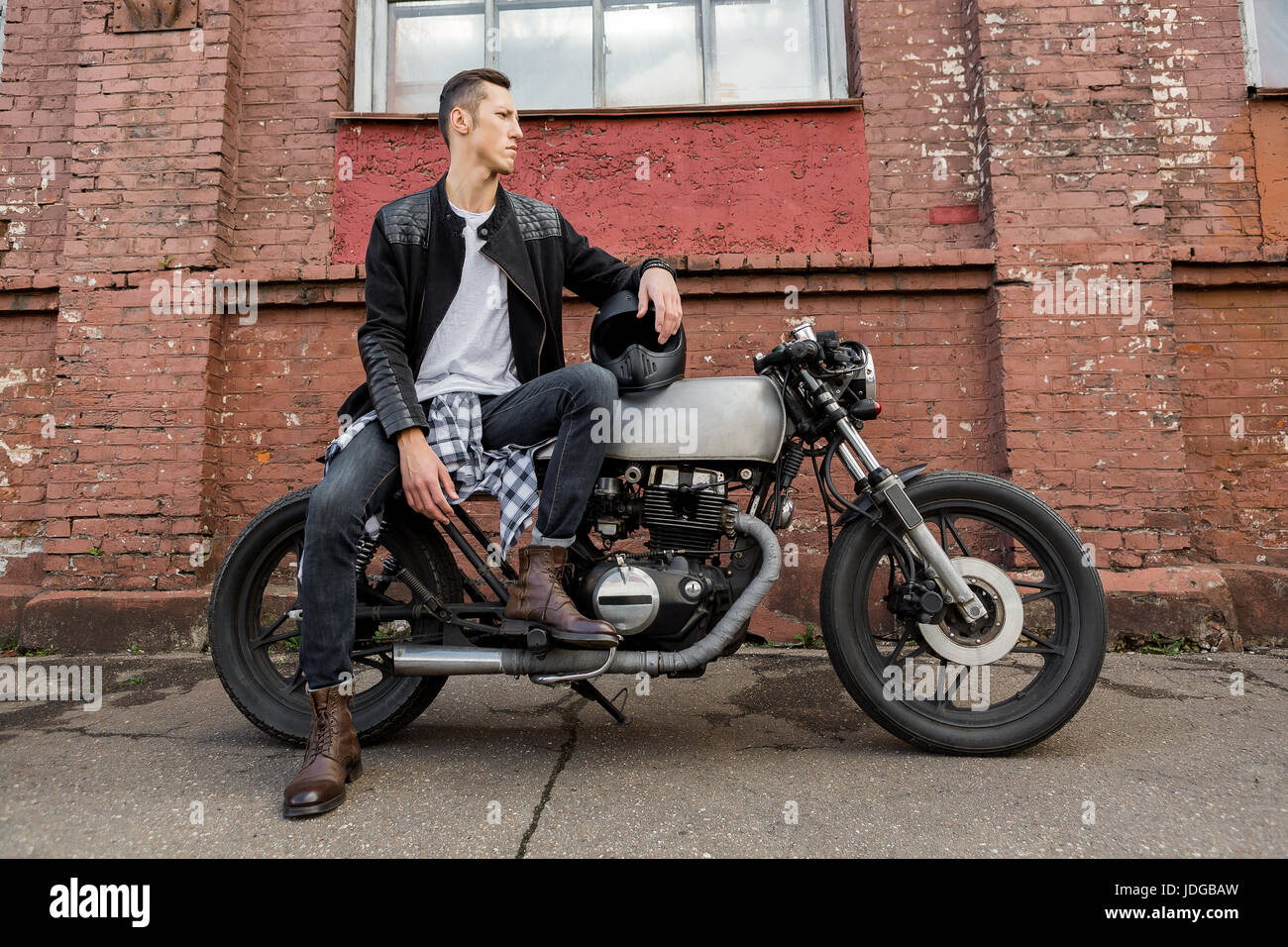 Handsome rider biker man in black leather jacket, jeans, boots and helmet  sit on classic style cafe racer motorcycle. Bike custom made in vintage  gara Stock Photo - Alamy