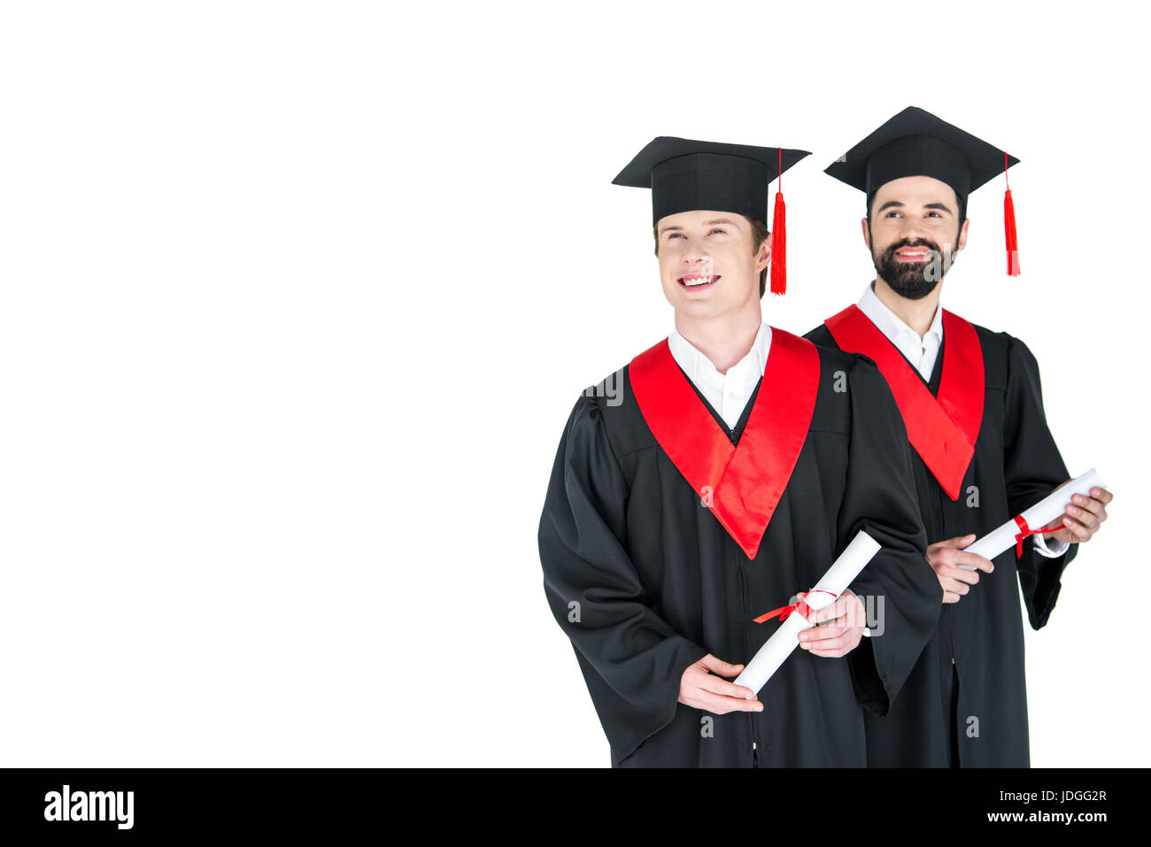 Two young men in academic caps holding diplomas and smiling on white Stock Photo