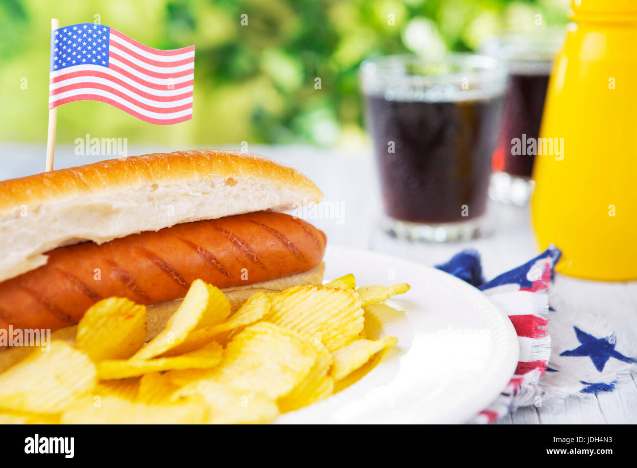 A tasty hot dog with potato chips on an outdoor table. Stock Photo