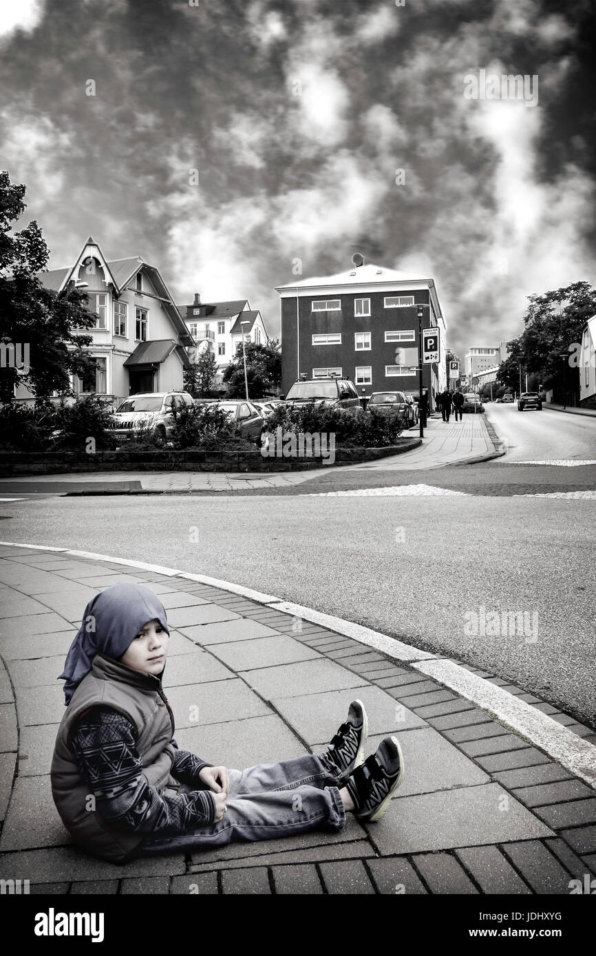 Little boy sitting on a sidewalk on a cold day in downtown Reykjavik, Iceland Stock Photo