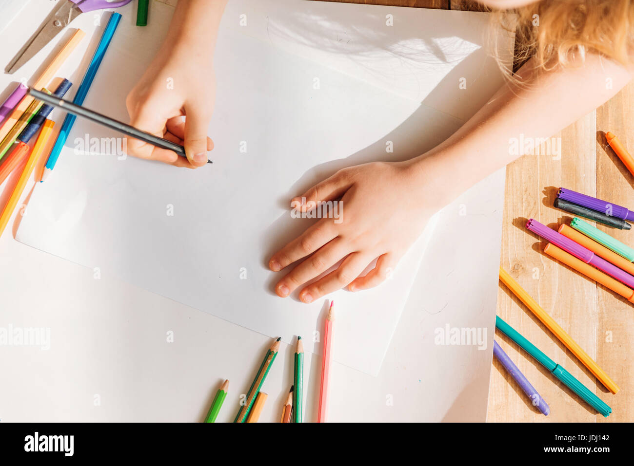 cropped view of cute kid drawing on paper with pencils while lying on ...