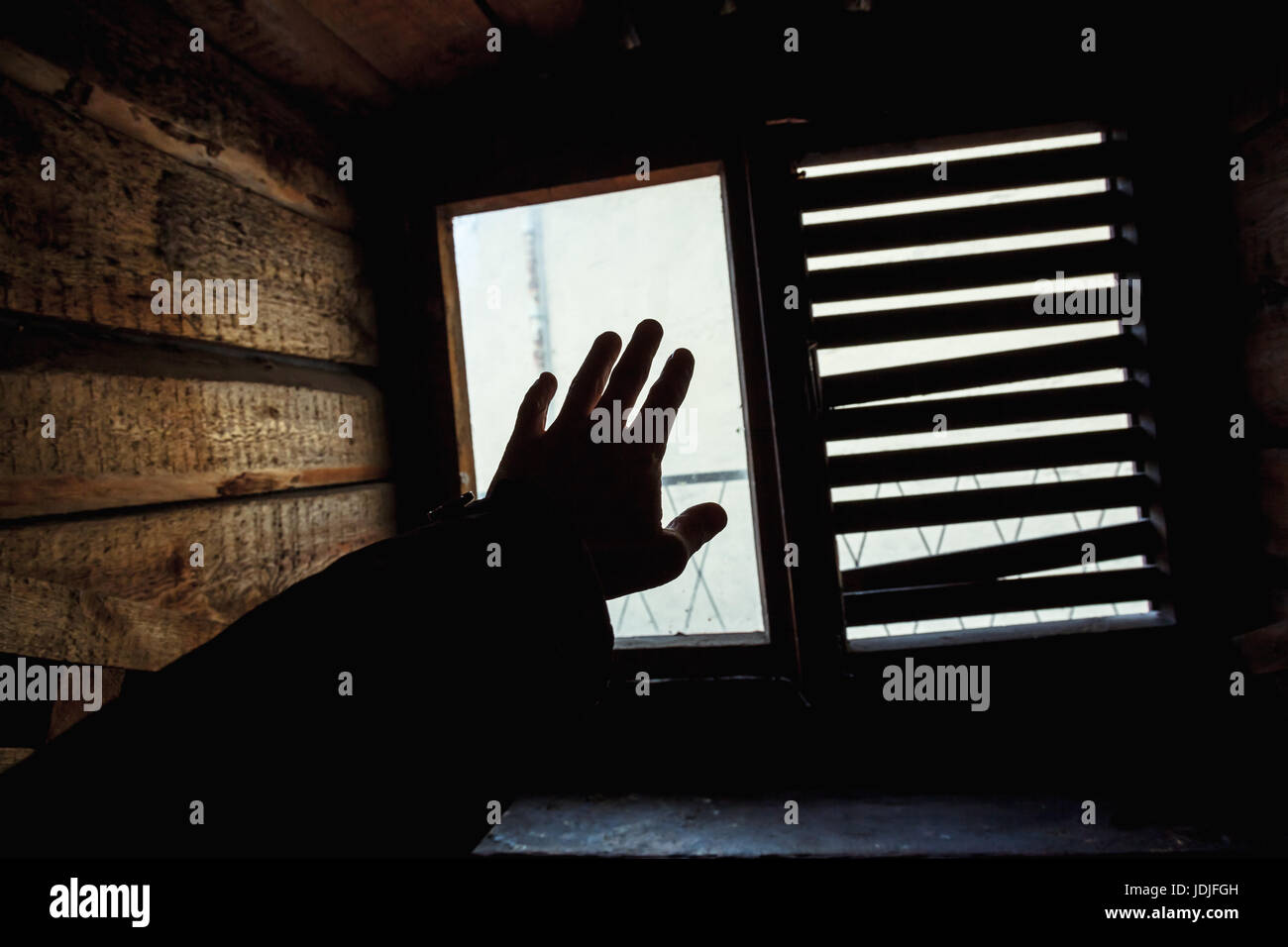 Male hand silhouette over small grungy window with shutters Stock Photo