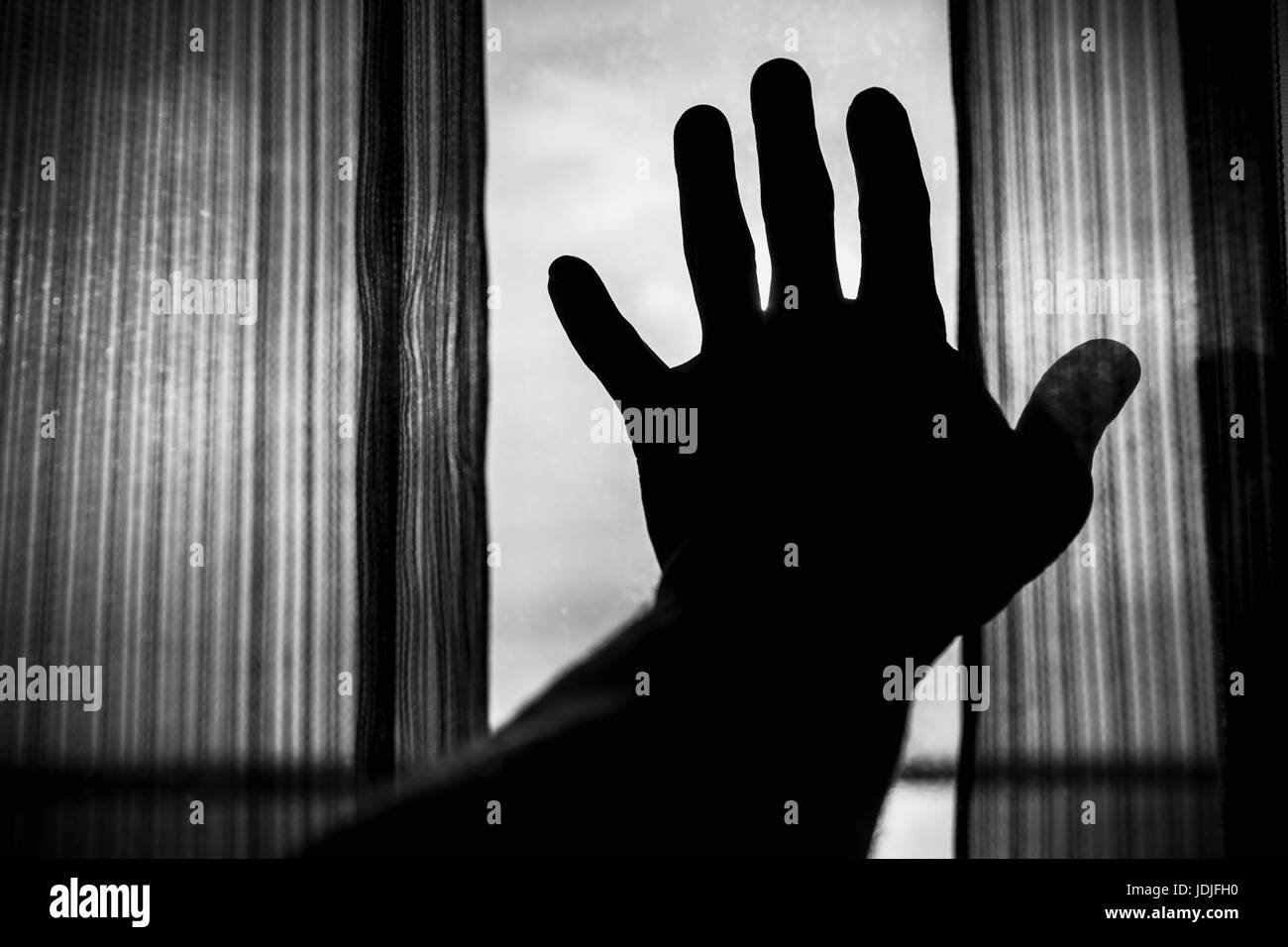 Male hand silhouette and tulle on window with bright daylight outside, black and white photo Stock Photo