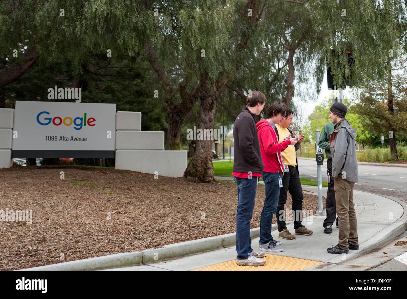 A group of millennial-age, young male technology workers stand in a group near signage for Google Inc at the Googleplex, the Silicon Valley headquarters of search engine and technology company Google Inc, Mountain View, California, with several checking text messages on their cellphones, April 7, 2017. Stock Photo