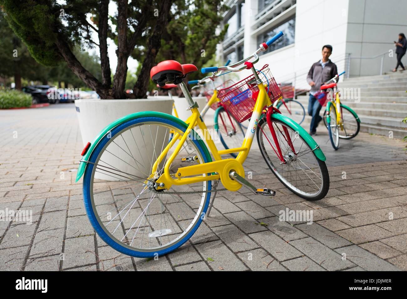 Closeup of a Google Bike, with a Google staff member approaching in the background, at the Googleplex, headquarters of Google Inc in the Silicon Valley town of Mountain View, California, April 7, 2017. Stock Photo