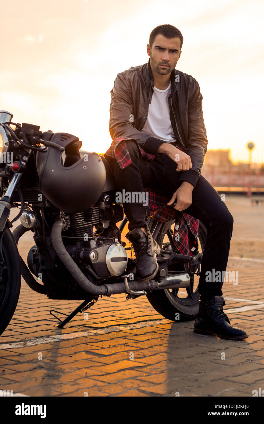 Handsome rider guy with beard and mustache in black leather biker jacket,  boot and jeans sit on classic style cafe racer motorcycle. Bike custom made  Stock Photo - Alamy