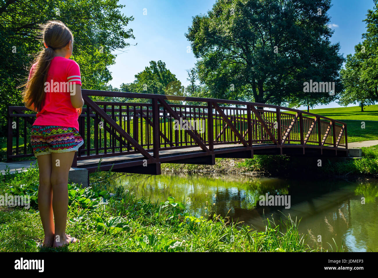 young girl standing next to a bridge over a creek Stock Photo