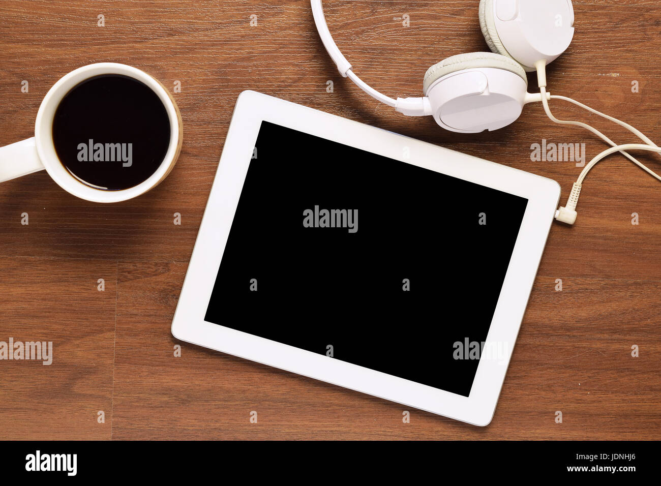 Top view of tablet computer, headphones and a cup of coffee on a wooden desk, with copyspace. Home office and lifestyle concept. Stock Photo