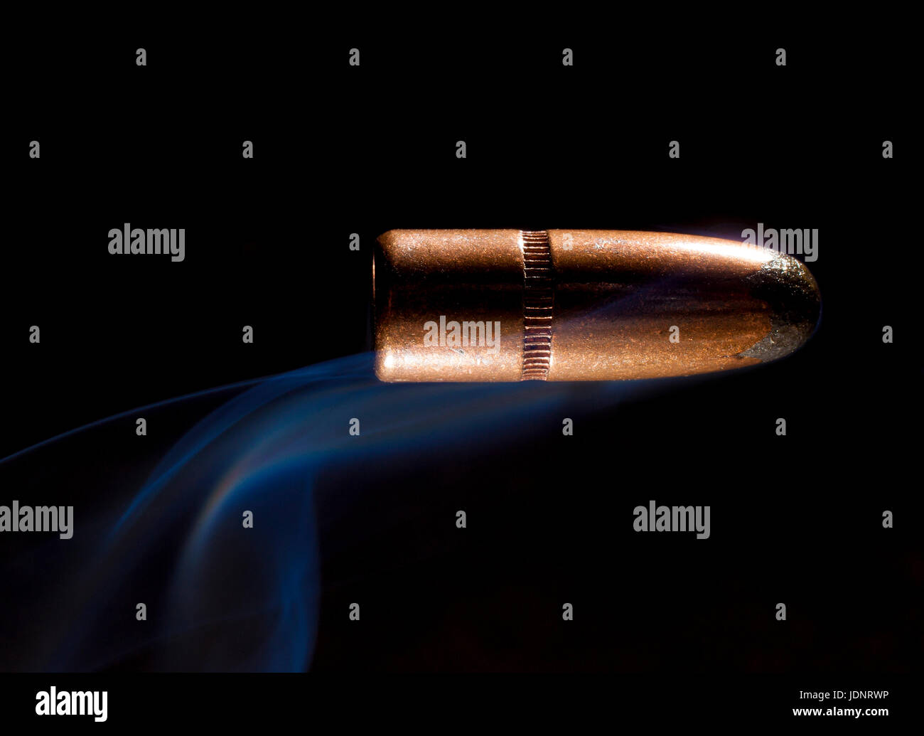 Bullet with copper plating and smoke behind with a black background ...