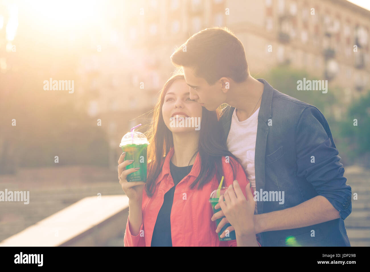 Teenagers drink fruit fresh from glasses. He hugs and kisses her. Couple in love. Romance of first love. Stock Photo