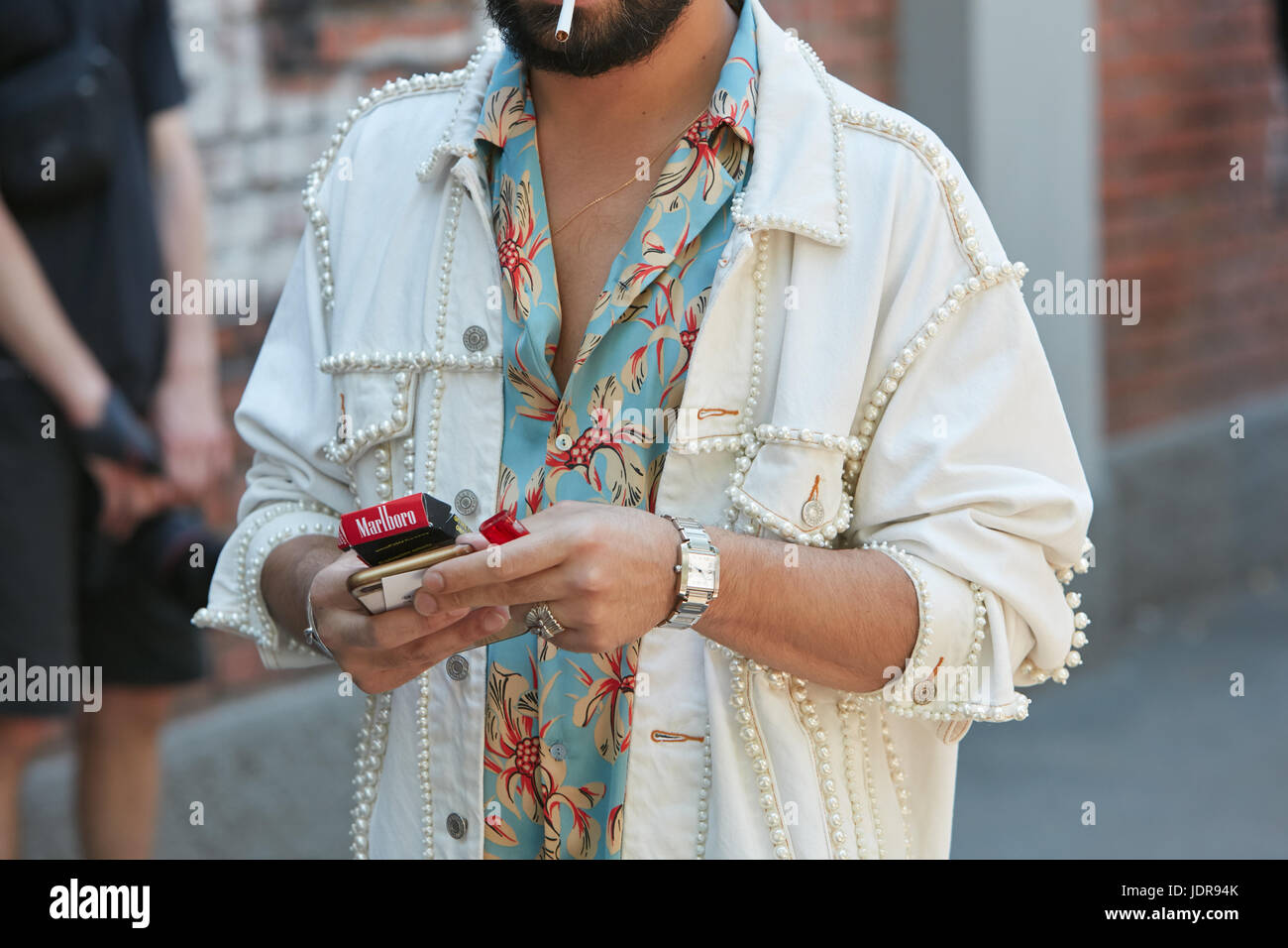 MILAN - JUNE 19: Man with white jeans jacket decorated with pearls and Cartier watch before Fendi fashion show, Milan Fashion Week street style on Jun Stock Photo