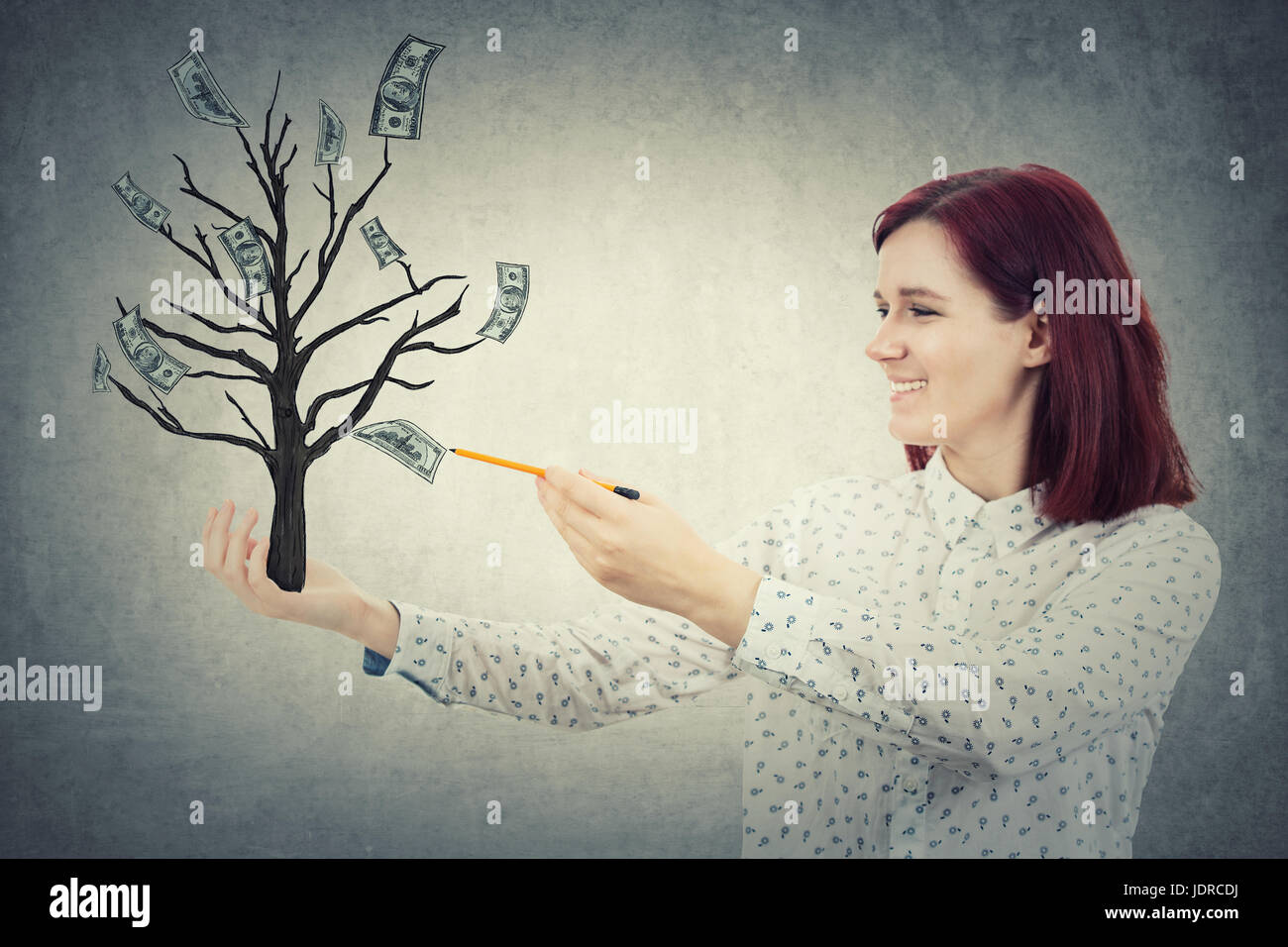 Young smiling girl with a pencil in her hand, drawing sketch a magic tree with dollars growing on it. The money tree, business success concept. Stock Photo