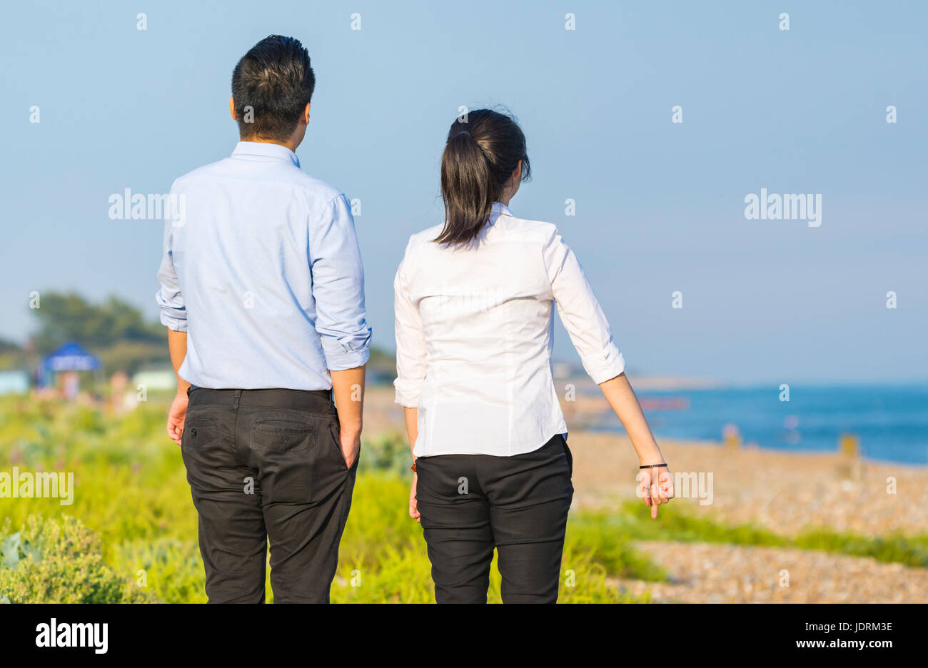 Young Asian couple dressed smartly walking on a beach on a warm summer evening in the UK. Stock Photo
