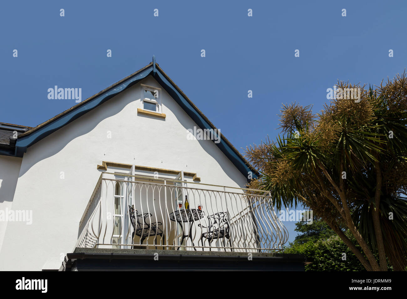 Balcony leading out of the bedroom a white walled house with table,glasses,wine,blue sky in mid summer. Stock Photo